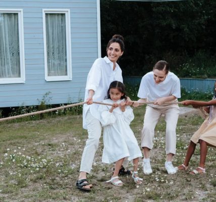 A happy family enjoys a game of tug of war in a grassy field by a house.