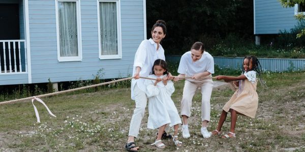 A happy family enjoys a game of tug of war in a grassy field by a house.