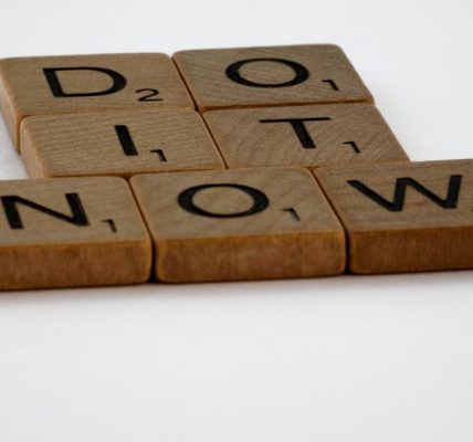 Wooden Scrabble tiles spelling 'Do It Now' on a white background. Motivational concept.