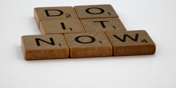Wooden Scrabble tiles spelling 'Do It Now' on a white background. Motivational concept.